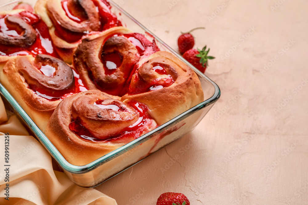 Baking dish with strawberry cinnamon rolls and napkin on beige background, closeup