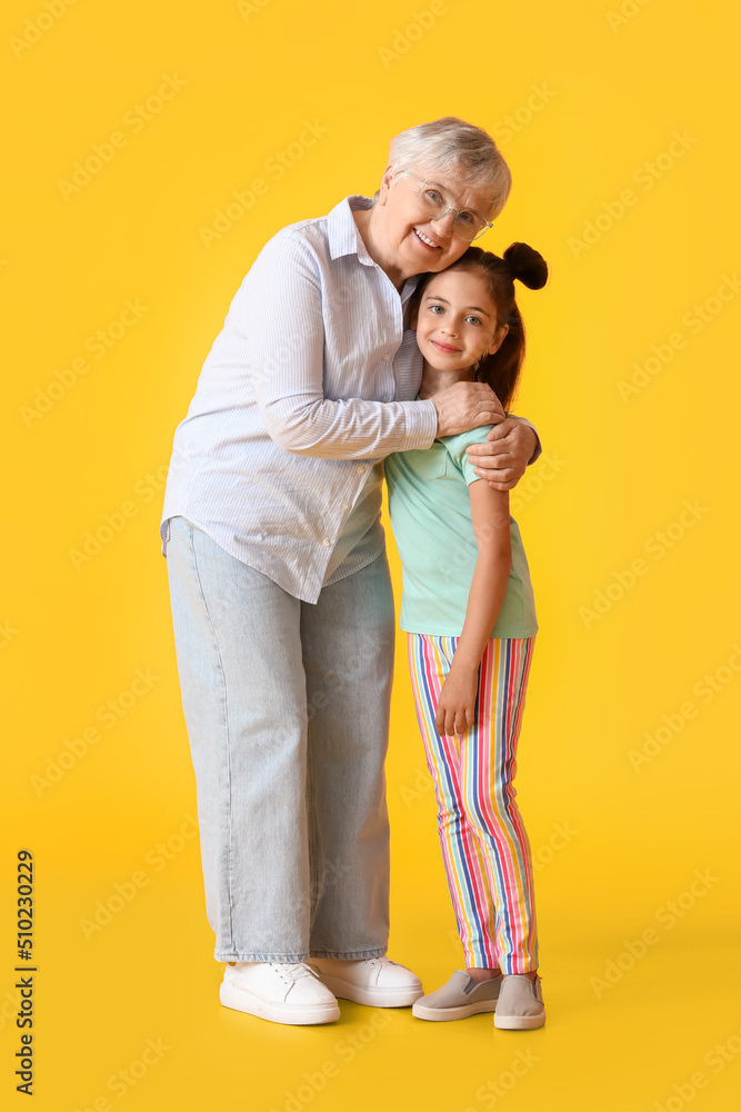 Little girl and her grandma hugging on yellow background