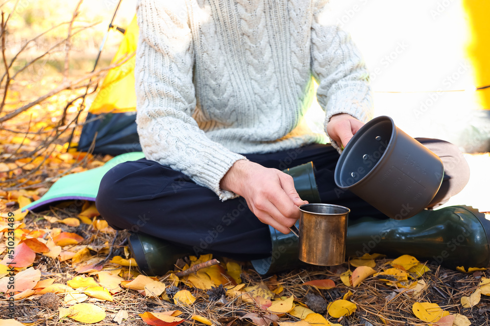 Male tourist pouring soup in metal mug during camping in forest