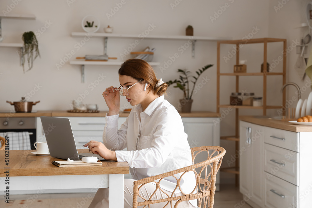 Young female freelancer working on laptop in kitchen