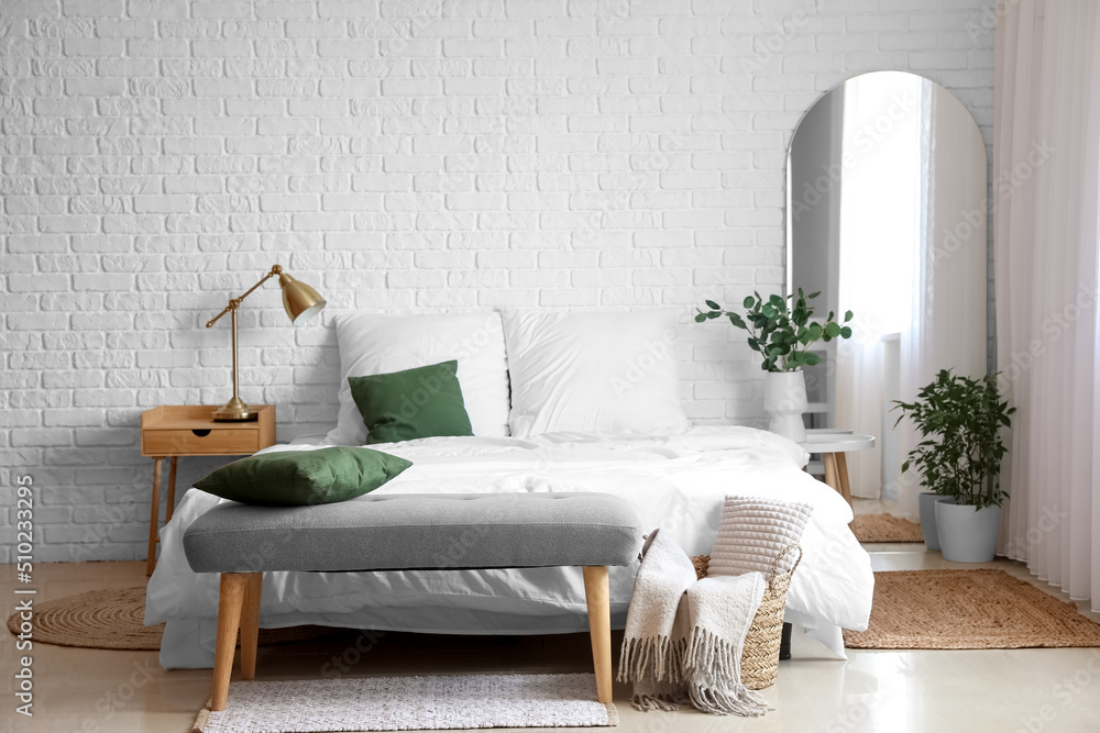 Interior of light bedroom with soft bench and houseplants