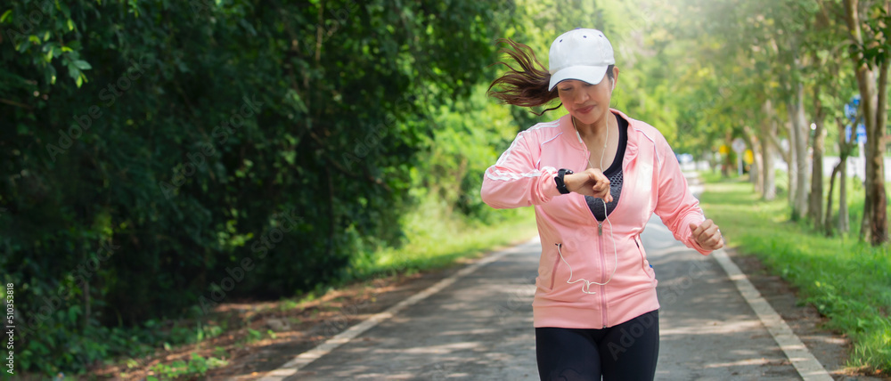 Asian  woman in sportswear Jogging running while checking heart rate at park on beautiful  day