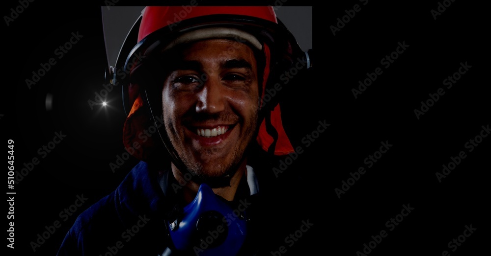 Caucasian firefighter wearing a helmet against spot of light and copy space on black background