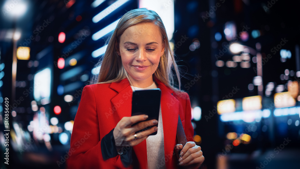 Beautiful Woman Standing, Using Smartphone on City Street with Neon Bokeh Lights Shining at Night. C