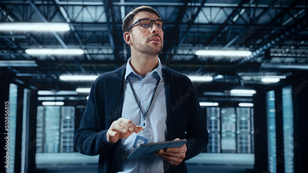 Male IT Specialist Walks Between Row of Operational Server Racks in Data Center. Engineer Uses Table