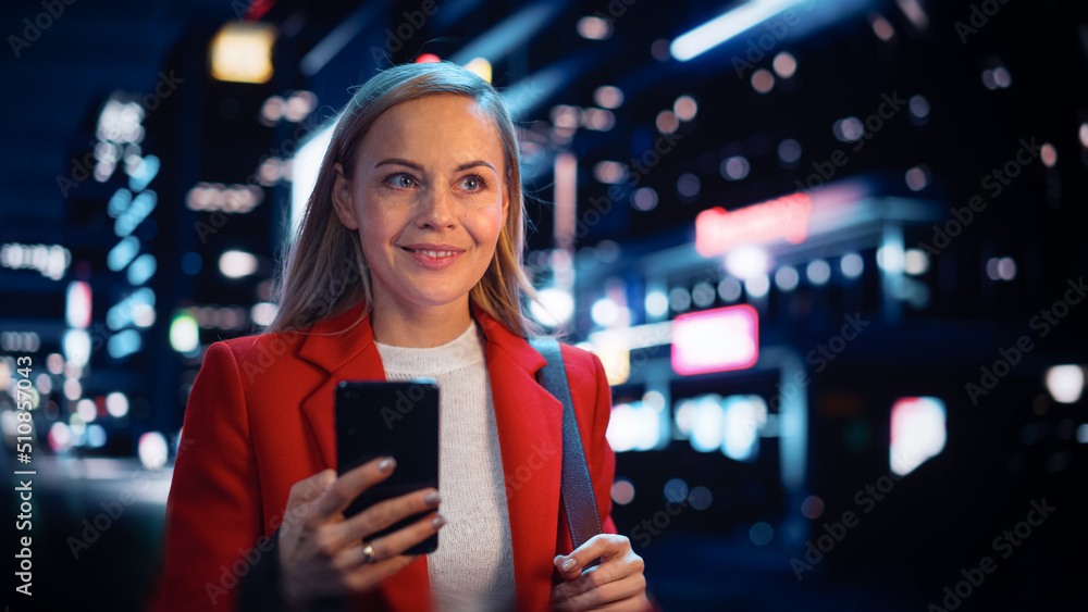 Portrait of a Beautiful Woman in Red Coat Walking in a Modern City Street with Neon Lights at Night.