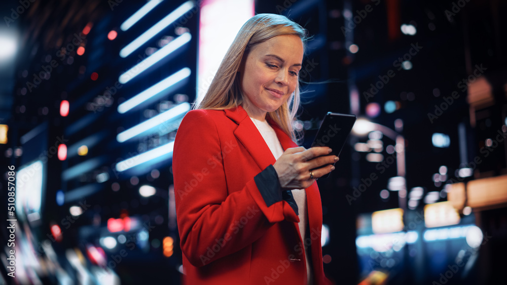 Beautiful Woman Standing, Using Smartphone on City Street with Neon Bokeh Lights Shining at Night. C