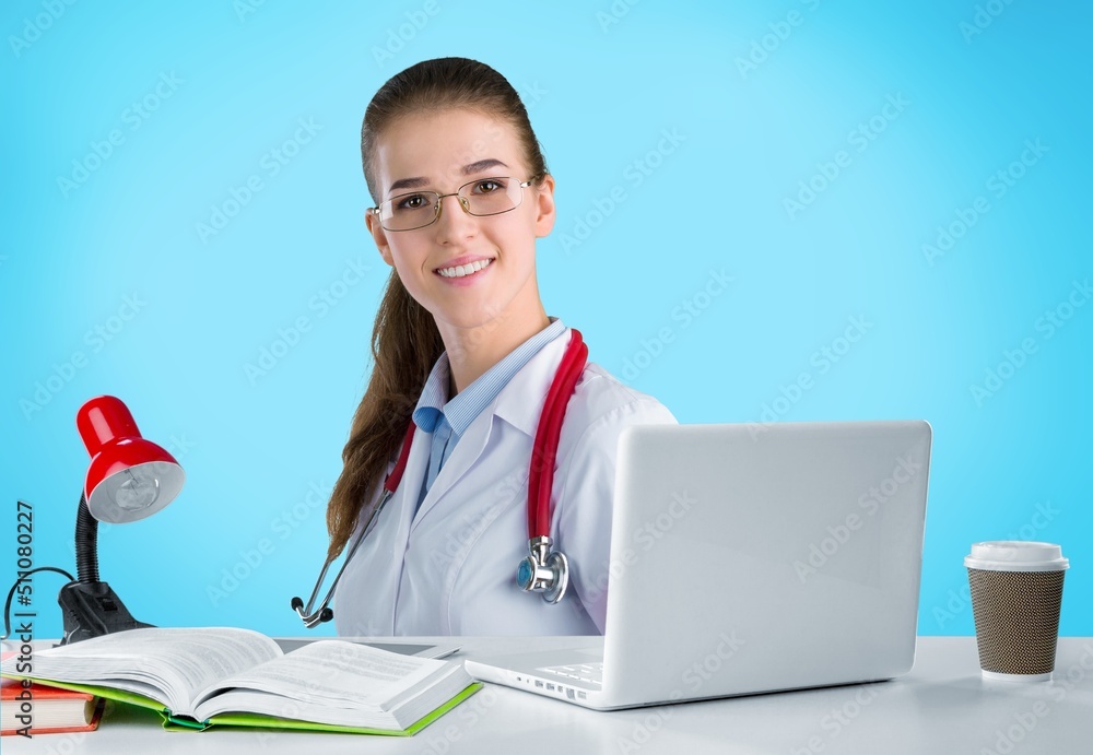 Attractive female doctor smiling while working with laptop in the consultation.