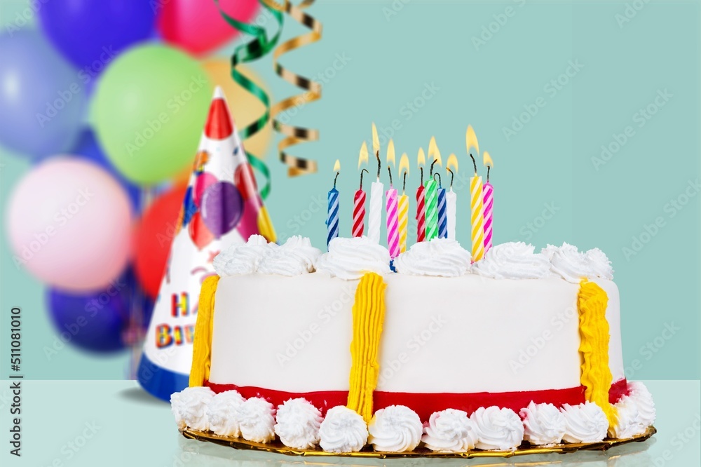 Sweet birthday cake with birthday candle, party hat, streamers and birthday balloons ready for a bir