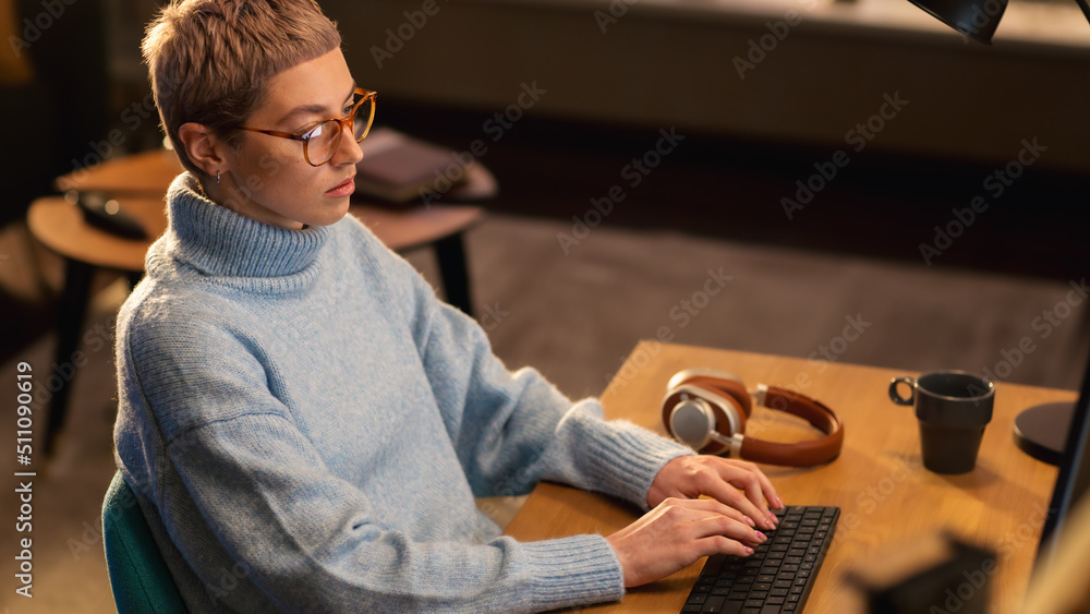 Young Beautiful Woman is Sitting Behind the Table Using Desktop Computer in Sunny Stylish Loft Apart