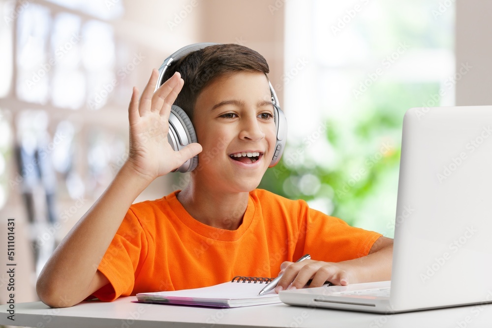 Joyful boy teenager using laptop at home, sitting at table among books and notebooks