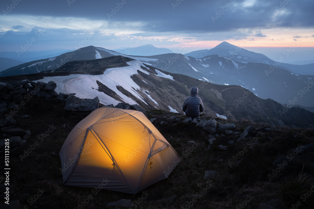 Grey tent lighted from the inside by a flashlight against the backdrop of an incredible mountain lan