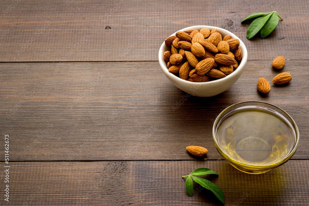 Sweet almond oil in glass jar and almond seeds with green leaf