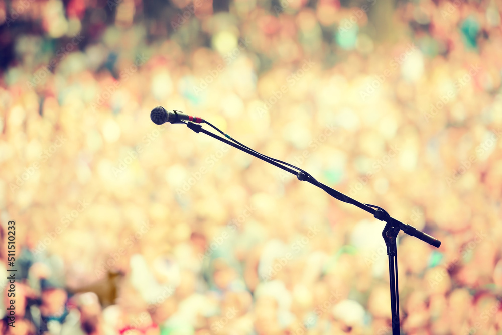 Ready to rock. A microphone on a stand on an empty stage with the audience in the background.