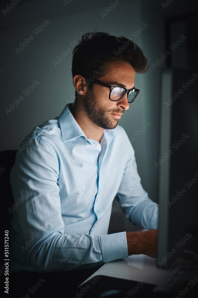 Powering through the night to get ahead. Shot of a young businessman working late on a computer in a