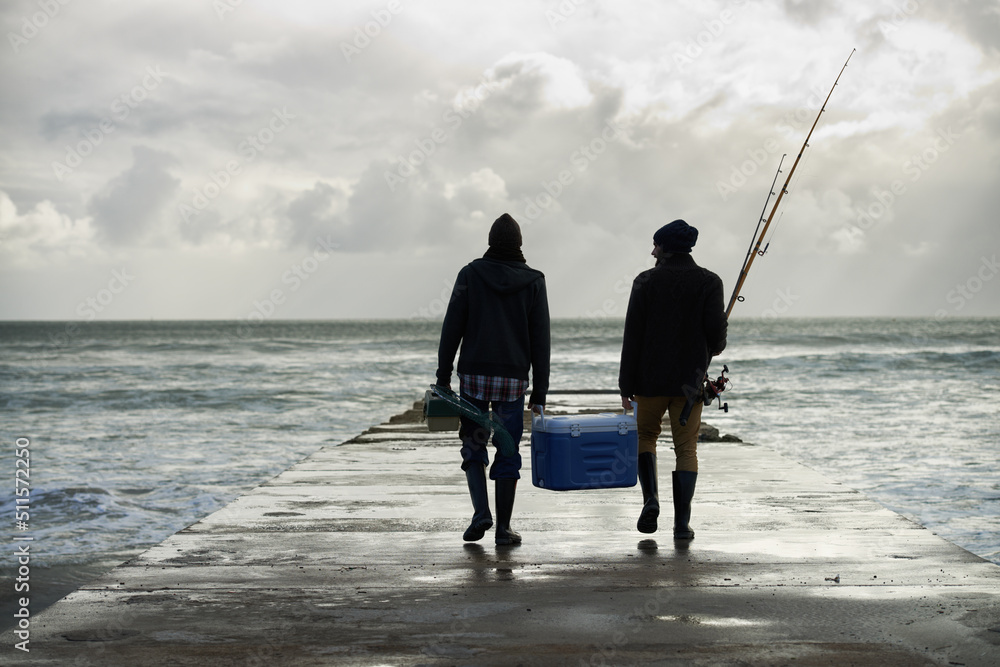 Carrying home their catch. Shot of two young men fishing at the ocean in the early morning.