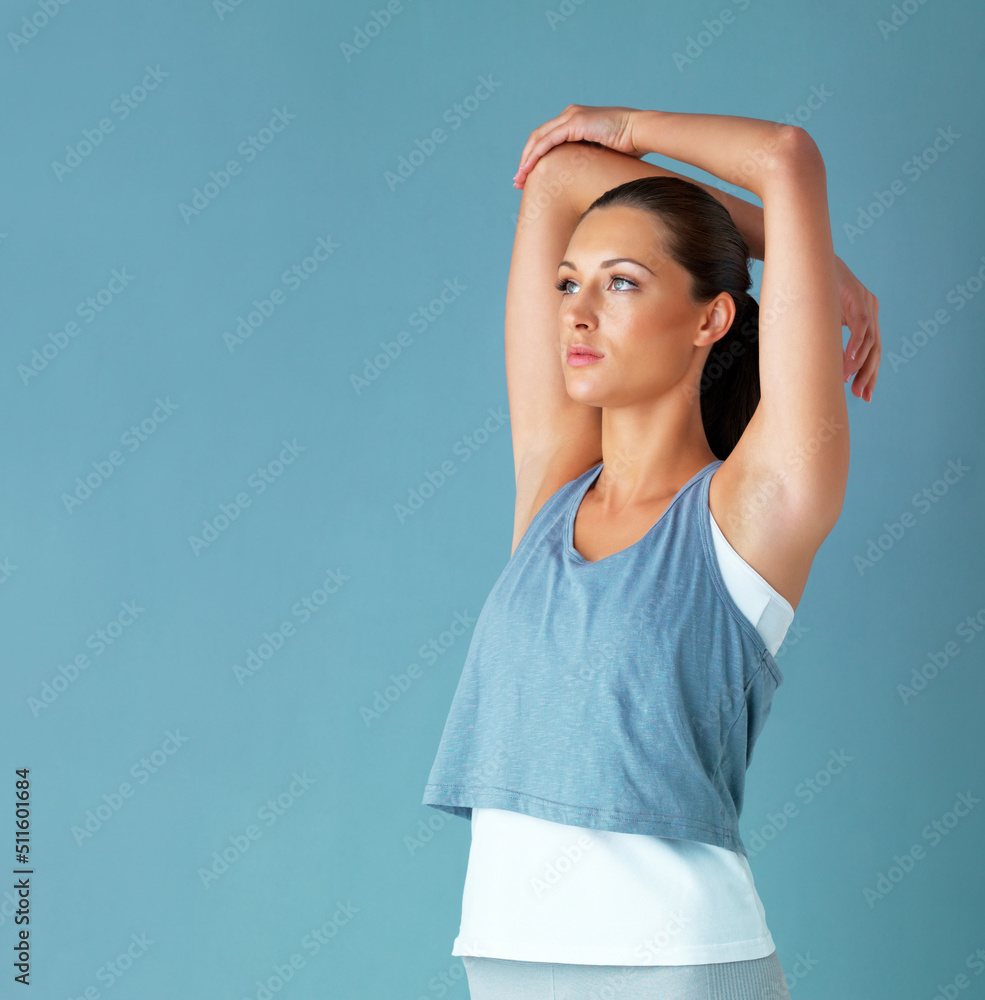 Getting prepped for a workout. Studio shot of a healthy young woman warming up against a blue backgr