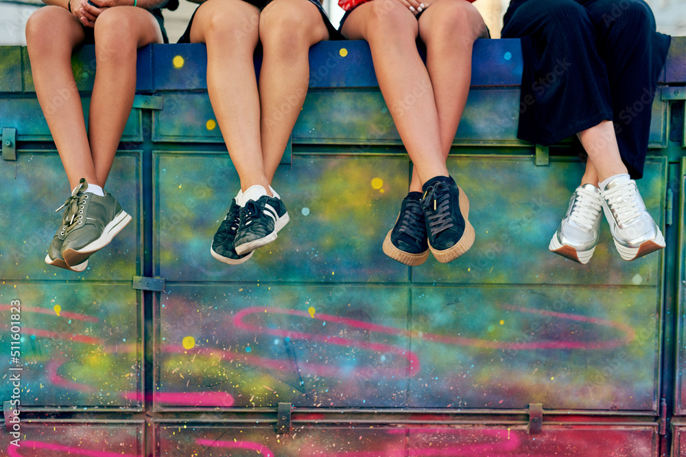 Take a seat. Cropped shot of four unrecognizable girlfriends sitting on a graffiti wall in the city.