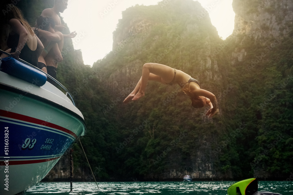 Live life with no regrets. Shot of a young woman doing a backflip off a boat while her friends watch