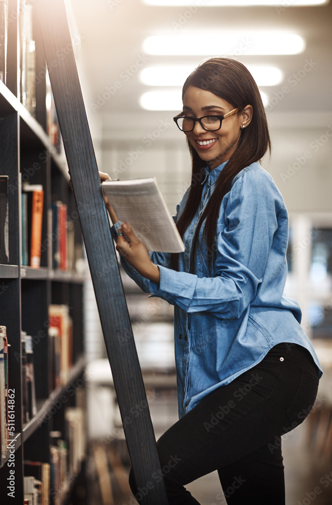 My professor recommended this one. Shot of a university student using a ladder to reach a book in th