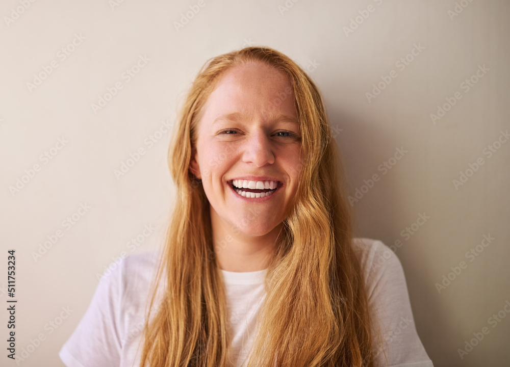 Laugh at yourself, life is short. Shot of a young woman smiling and standing against a wall at home.