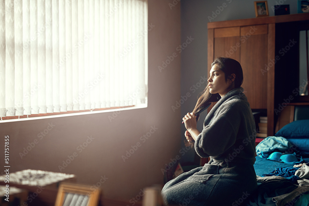 Thinking about the day that lies ahead. Shot of a young woman brushing her hair while sitting on her