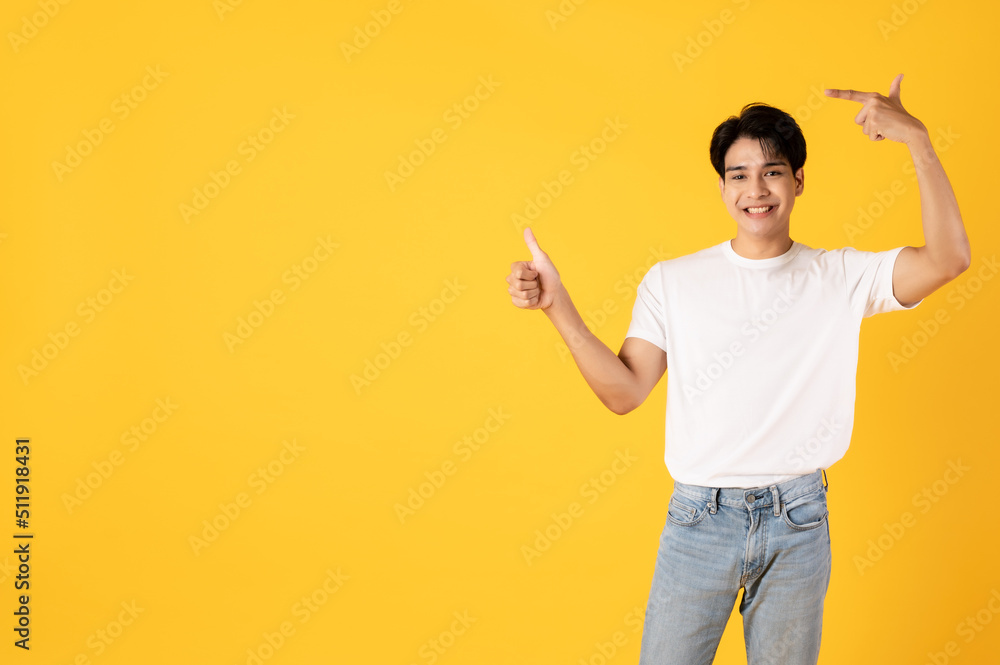 Smiling young asian teenage man wearing white shirt and jeans on yellow background giving thumbs up 