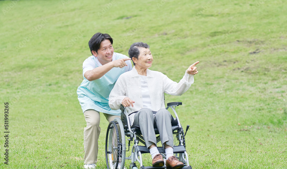 看護師と屋外を車椅子に乗って散歩する高齢者女性