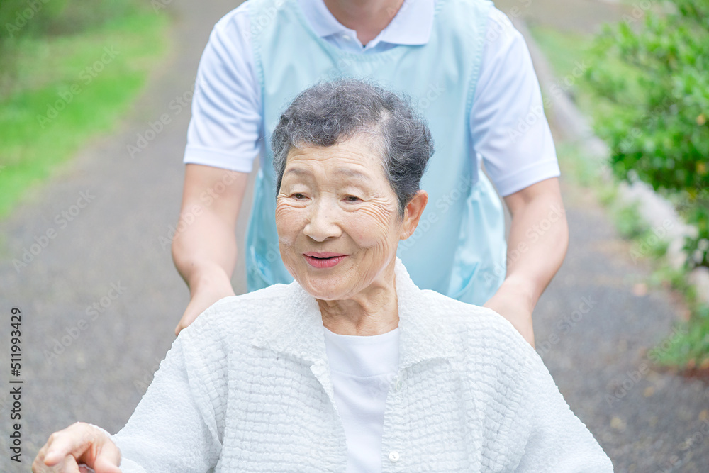 看護師と屋外を車椅子に乗って散歩する高齢者女性