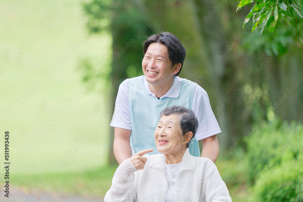 看護師と屋外を車椅子に乗って散歩する高齢者女性