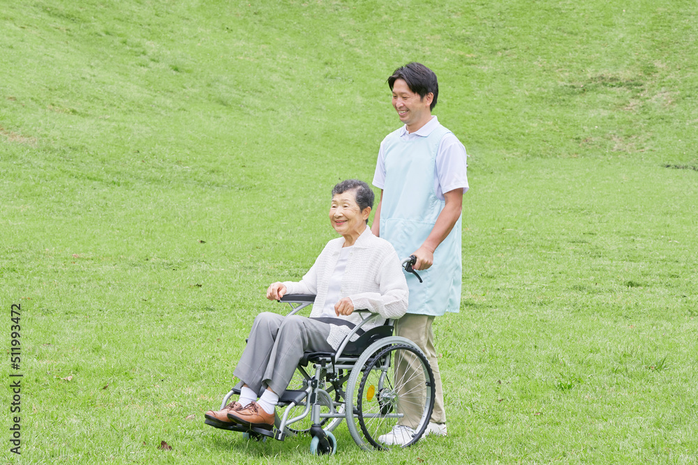 看護師と屋外を車椅子に乗って散歩する高齢者女性