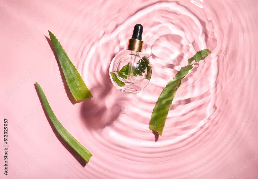 Bottle of natural serum and aloe leaves in water on pink background