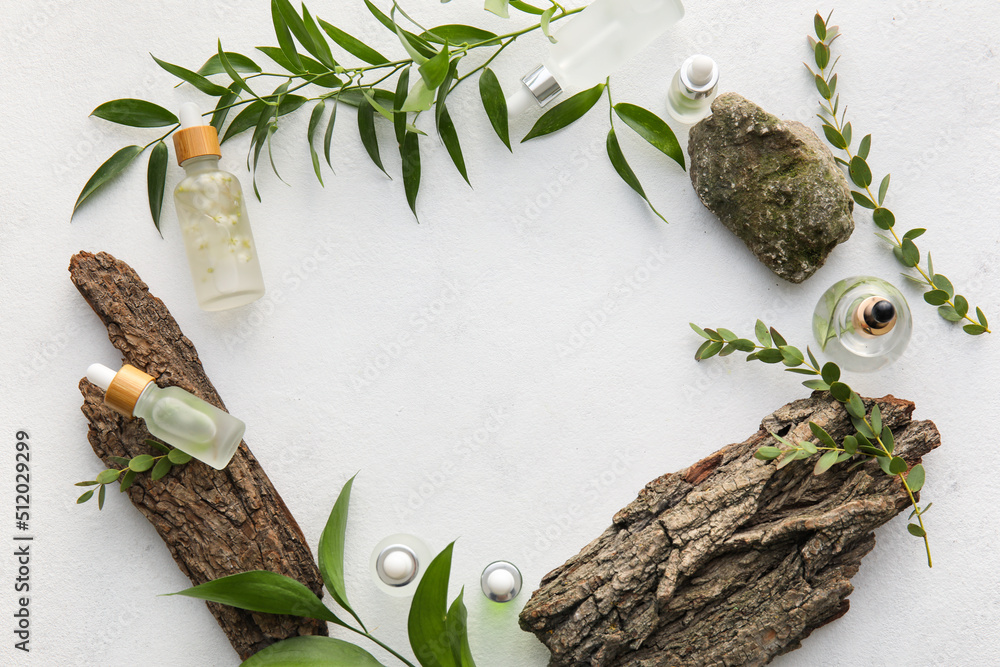 Frame made of bottles with natural serum, plant leaves and tree barks on light background