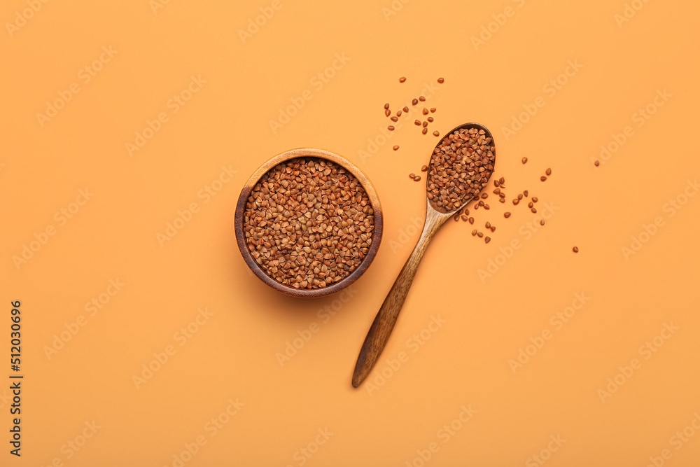 Wooden bowl and spoon with buckwheat grains on color background