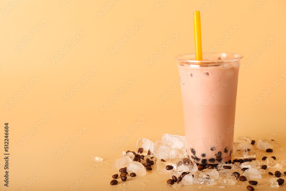 Plastic cup of tasty bubble tea with coffee beans and ice cubes on color background