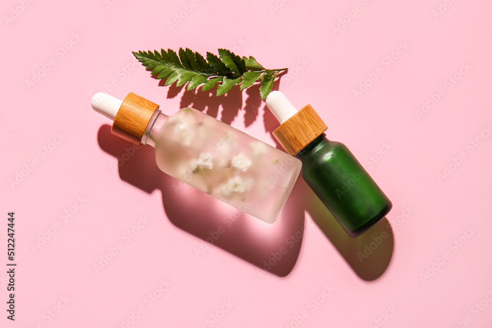 Bottles of natural serum and fern leaf on pink background