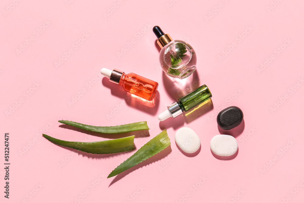 Composition with bottles of natural serum, spa stones and aloe leaves on pink background