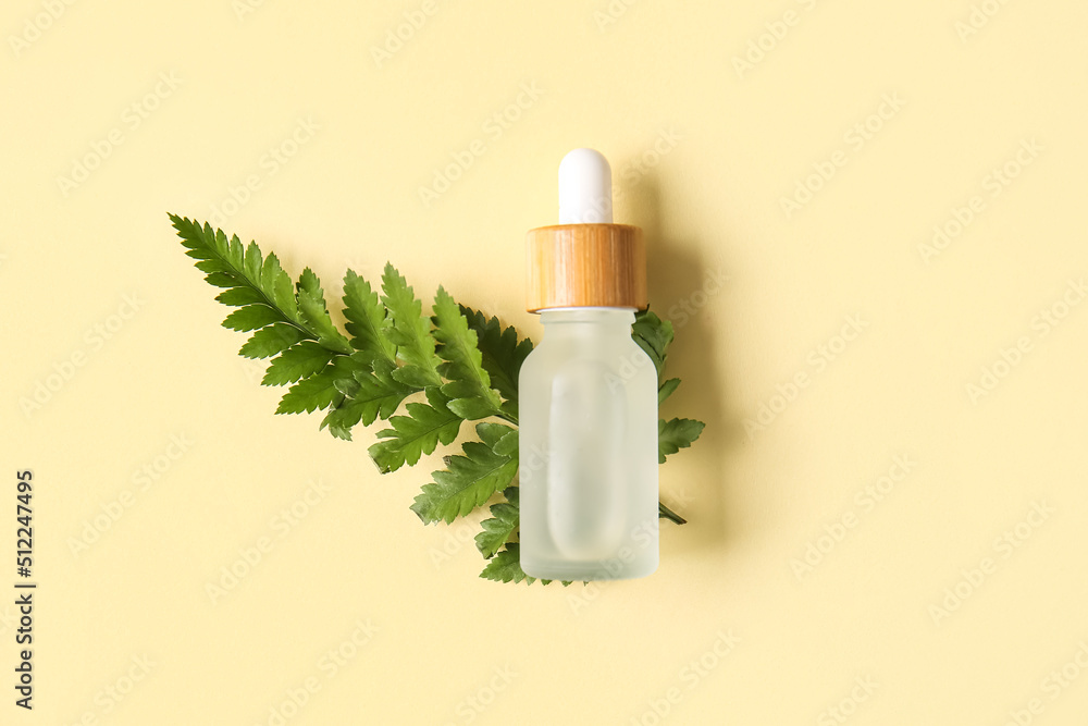 Bottle of natural serum and fern leaf on color background