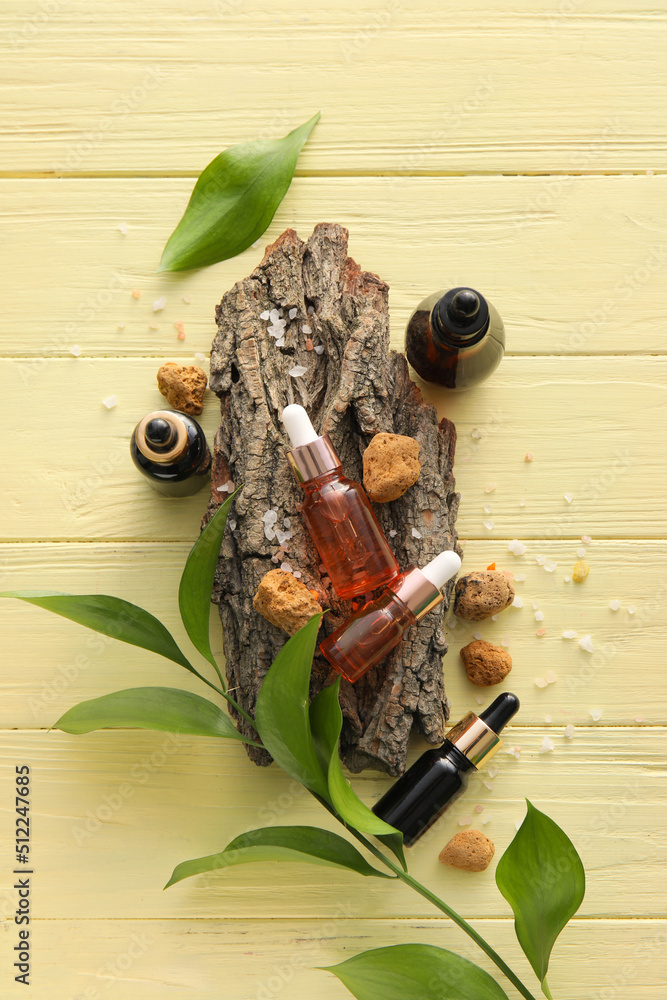 Bottles of natural serum, stones, tree bark and plant leaves on yellow wooden background