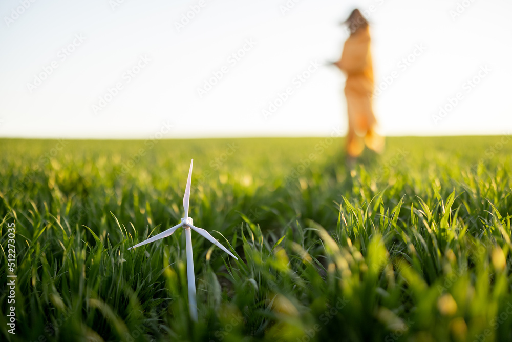 Toy wind generator on green wheat field with person behind on sunset. Concept of alternative energy 