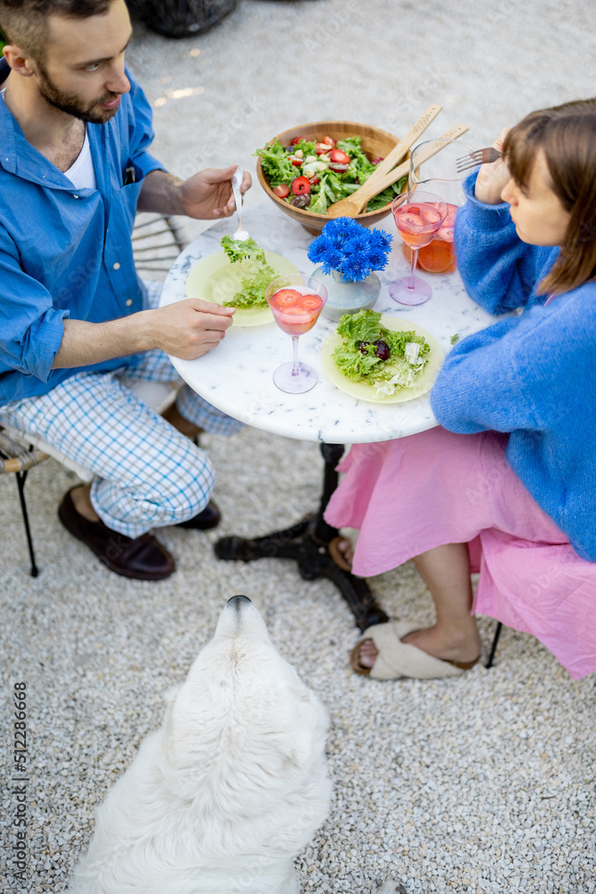 Young and cheerful couple eat healthy salad and drink summer drink while sitting together by a round