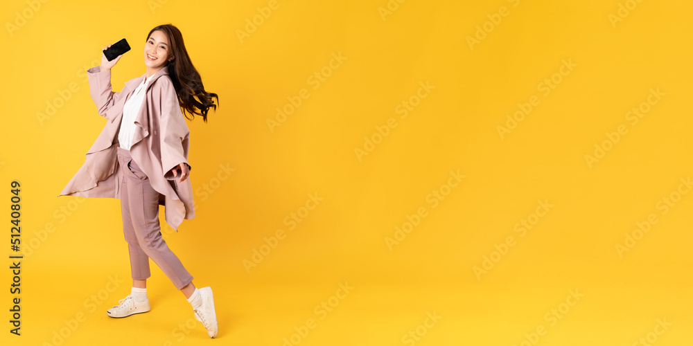 Smiling asian woman white shirt and blazer on yellow background holding smart phone