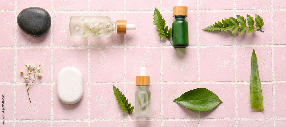 Composition with cosmetic serum, green leaves and spa stones on pink background