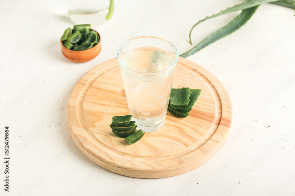 Board with glass of aloe juice and leaves on white background