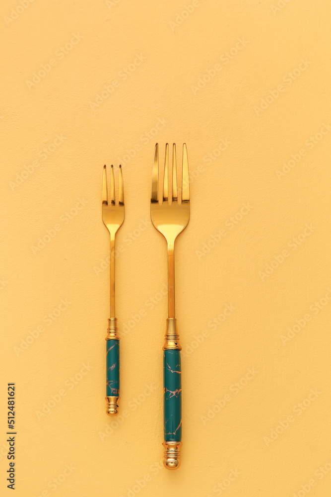 Stylish stainless steel forks on yellow background