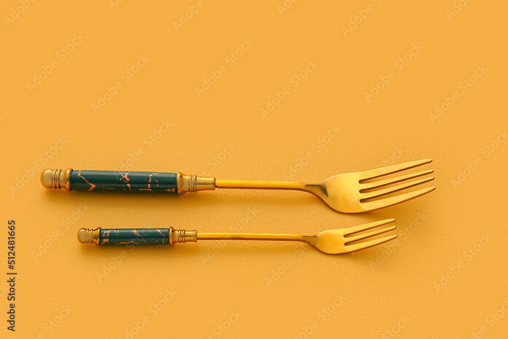 Stylish stainless steel forks on yellow background