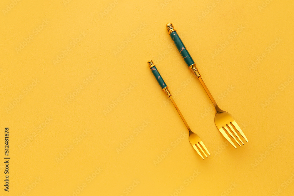 Stylish stainless steel forks on yellow background