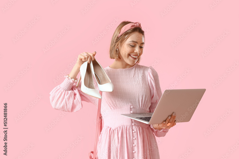 Young woman with laptop and new heels on pink background. Online shopping