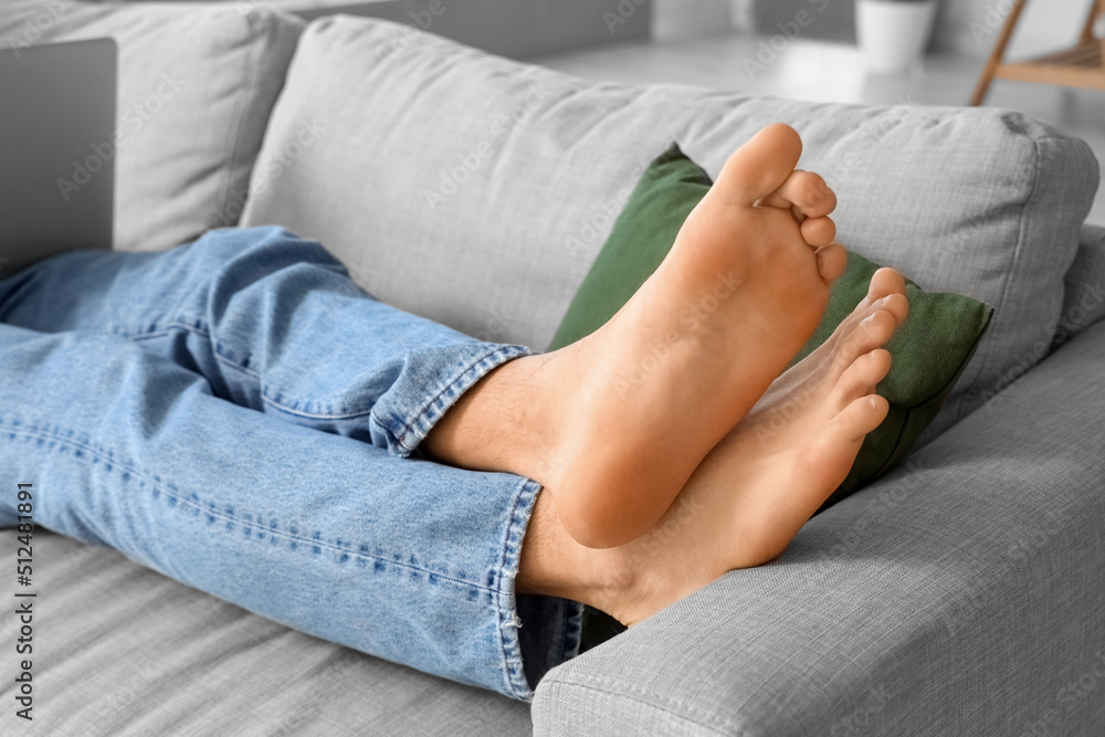 Young barefoot man lying on sofa at home, closeup