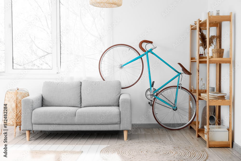 Interior of light living room with bicycle, grey sofa and wooden shelving unit